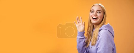 Photo for Waist-up friendly lucky cute blond girl waving palm happily smiling turning camera greet friend say hello hi see familiar person welcoming newcomers joyfully, standing orange background. - Royalty Free Image