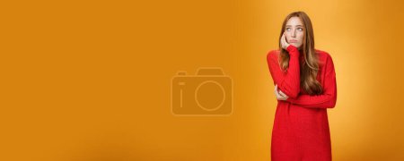 Photo for Lifestyle. Sorrow and upset lonely woman leaning head on palm in upset pose looking gloomy at upper left corner as remembering unhappy story or being bored standing uneasy over orange wall. - Royalty Free Image