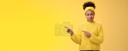 Attractive peeky glamour african-american girlfriend express dislike doubt frowning cringing aversion disappointed pointing left high hopes ruined, look disdain feel dismay yellow background.