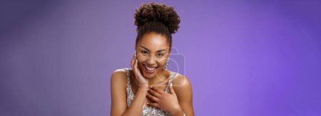 Photo for Close-up flirty cheeky young stylish african american. woman attend luxurious party in silver dress giggling receive compliment smiling gladly touch chest grateful standing pleased blue background. - Royalty Free Image