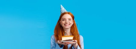 Photo for Celebration, holidays and happiness concept. Cheerful tender and feminine, lovely redhead woman in b-day cap, holding piece cake celebrating birthday, blow-out candle and make wish. - Royalty Free Image