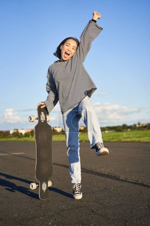 Téléchargez les photos : Excité asiatique fille danse, debout avec skateboard, patinage sur longboard et crier insouciant. - en image libre de droit