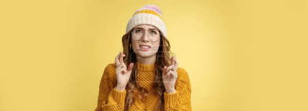 Photo for Worried cute girl nerd hope pass exam standing nervous cross fingers good luck frowning grimacing look up praying supplicating anticipating results anxiously, wearing glasses, yellow background. - Royalty Free Image