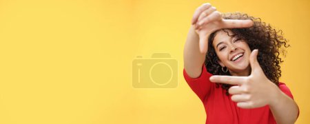Foto de Estilo de vida. Retrato de optimista estudiante feliz y creativa imaginando su nuevo apartamento como manos extendidas y mostrando marcos gesto sonriendo a través de ella en la cámara divertida y despreocupada sobre amarillo - Imagen libre de derechos