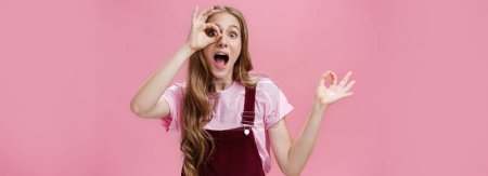 Photo for Zero regrets after buying new dress. Charismatic charming young girlfriend in overalls showing okay or cirle over eye looking through it amazed and excited at camera having small tattoos and scars. - Royalty Free Image