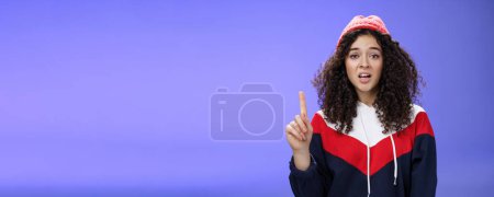 Photo for Rule number one do not mess with me babe. Portrait of swag and cool stylish young curly-haired woman in winter beanie showing index finger in prohibition or warning gesture over blue background. - Royalty Free Image