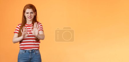 Téléchargez les photos : Putain, ça pue. Dégoûté rousse difficile femme bloquant signe lever les mains vers le haut défensif, grimaçant, grincer de l'aversion odeur horrible, montrer refus rejetant offre dégoûtante, stand fond orange. - en image libre de droit