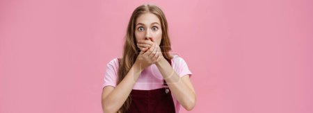 Photo for Lifestyle. Waist-up shot of shocked speechless pretty young girl in overalls with make-up covering mouth with palms from overreacting on terrible news witnessing accident nervously over pink - Royalty Free Image