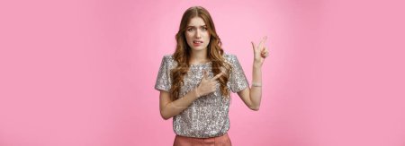 Photo for Dispelased insecure awkward young glamour rich girl dress-up party disappointed dislike place cringing aversion disgust pointing left questioned troubled, concerned standing pink background. - Royalty Free Image