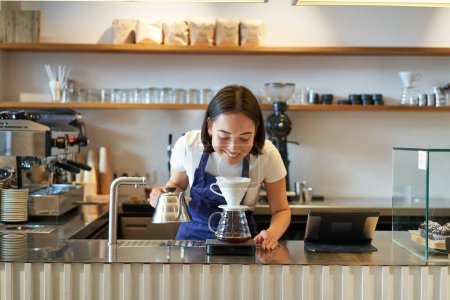 Photo for Smiling asian girl barista, working in cafe, brewing coffee v60, preparing order behind counter. - Royalty Free Image