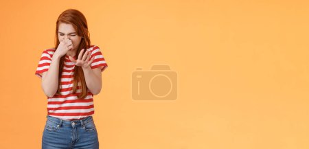 Photo for Gosh it stinks. Reluctant disgusted redhead woman raise hand block dislike gesture shut nose, cringe from aversion dislike, puke from reek bad smell, stand orange background disappointed. Copy space - Royalty Free Image