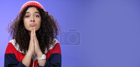 Photo for Lifestyle. Close-up shot of cute feminine girlfriend begging bring her favorite sweets holding hands in pray folding lips and gazing with angel innocent gaze at camera as asking favour over blue - Royalty Free Image