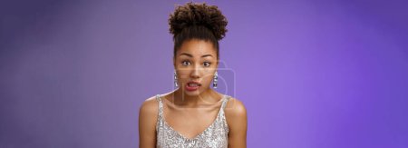 Photo for Awkward cute african-american woman. in silver glamour dress clench teeth look worried complicated say oops make mistake accidently spill drink standing unsure insecure blue background. - Royalty Free Image
