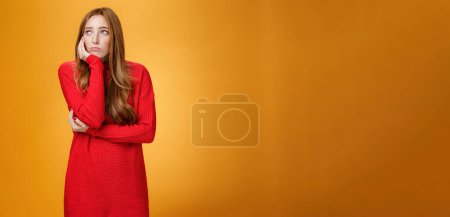 Photo for Lifestyle. Sorrow and upset lonely woman leaning head on palm in upset pose looking gloomy at upper left corner as remembering unhappy story or being bored standing uneasy over orange wall. - Royalty Free Image