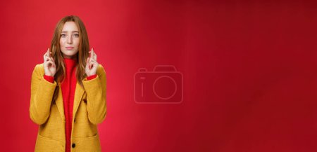 Photo for Girl having faith everything be fine cross fingers for good luck as supplicating, making wish looking hopeful at camera anticiapting miracle and dream come true against red background. - Royalty Free Image