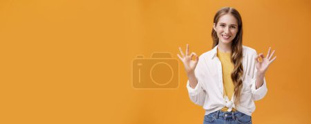 Photo for Lifestyle. Indoor shot of assertive and assured charming stylish woman in blouse over t-shirt and accessories showing okay gesture with delighted self-assured smile giving being ok against orange wall - Royalty Free Image