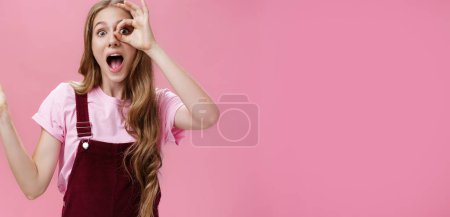 Photo for Zero regrets after buying new dress. Charismatic charming young girlfriend in overalls showing okay or cirle over eye looking through it amazed and excited at camera having small tattoos and scars. - Royalty Free Image