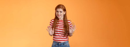 Photo for Reluctant bothered cute redhead girl apologizing make stop refusal sign, hold hands block, grimacing, cringe unwilling participate, rejecting offer, stand orange background uncomfortable, step back. - Royalty Free Image