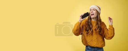 Photo for Carefree charming girl likes karaoke having fun listen favorite songs wearing wired earphones hold smartphone microphone singing out loud dancing enjoying spend time alone. Technology concept - Royalty Free Image