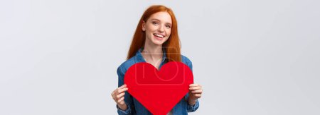Photo for Valentines day, romance and teenagers concept. Lovely and cute redhead girlfriend asking wanna go prom together with big red heart, confessing love, smiling joyfully, white background. - Royalty Free Image