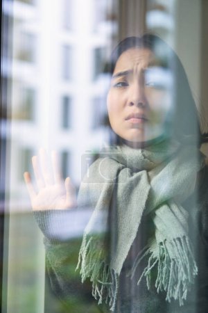 Foto de Asiática mujer se siente mal, se queda en casa, mira fuera de la ventana con celoso, cara angustiada, quiere salir fuera, pero atrapado frío. - Imagen libre de derechos