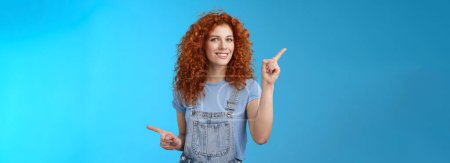 Photo for Lifestyle. Lively joyful good-looking 25s redhead curly-haired sassy girl summer positive mood dancing overalls pointing sideways up right index fingers directing promos store links smiling delighted. - Royalty Free Image