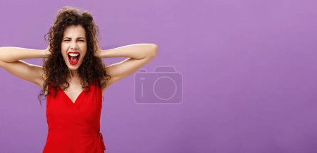 Téléchargez les photos : Ex-boyfriend spoilt woman formal event being outraged. and pissed yelling in fury holding hands on curly hair grimacing from anger standing over purple background in stylish evening red dress. - en image libre de droit