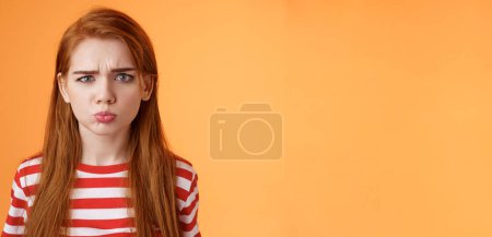 Photo for Childish offended cute redhead girl pouting, sulking upset, frowning, complain unfair situation, whining displeased, grimacing upset, act immature demand buy copy space orange background. - Royalty Free Image
