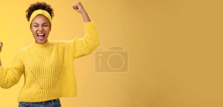 Photo for Active outgoing confident cheerful african-american female fan place bet hopefully yelling encourage team win standing raised fists victory celebrating gesture shouting proudly, yellow background. - Royalty Free Image