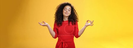 Photo for Charming dreamy and happy peaceful woman in red dress with curly hair standing in lotus pose with mudra orbs or zen gesture and closed eyes, meditation relieving stress, feeling unbothered. Body - Royalty Free Image