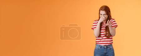 Photo for Gosh it stinks. Reluctant disgusted redhead woman raise hand block dislike gesture shut nose, cringe from aversion dislike, puke from reek bad smell, stand orange background disappointed. Copy space - Royalty Free Image