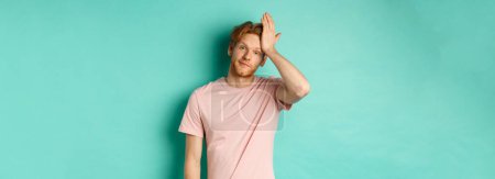 Photo for Annoyed and bothered redhead male model showing facepalm gesture, standing over mint background. - Royalty Free Image