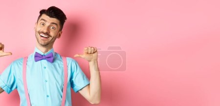 Photo for Cheerful smiling man with moustache and bow-tie, pointing at himself and self-promoting, standing happy over pink background in suspenders. - Royalty Free Image