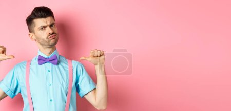 Photo for Serious and funny young man trying look cool, pointing at himself to self-promote, being a professional, standing over pink background. - Royalty Free Image