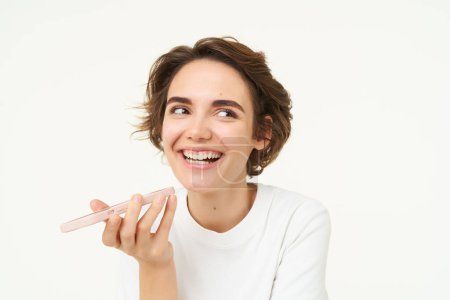 Photo for Laughing, happy woman talking on speakerphone, holding phone near mouth, recording voice message on smartphone, standing over white background. - Royalty Free Image
