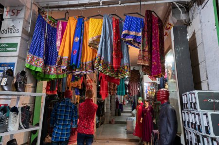 Photo for Jodhpur, Rajasthan, India - 19.10.2019 : Rajasthani womens clothes being sold in a shop at famous Sardar Market and Ghanta ghar Clock tower in the evening. - Royalty Free Image