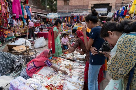 Photo for Jodhpur, Rajasthan, India - 20.10.2019 : White necklaces, gold plated earrings and ornaments are being sold to young female customers at famous Sardar Market and Ghanta ghar Clock tower in Jodhpur. - Royalty Free Image