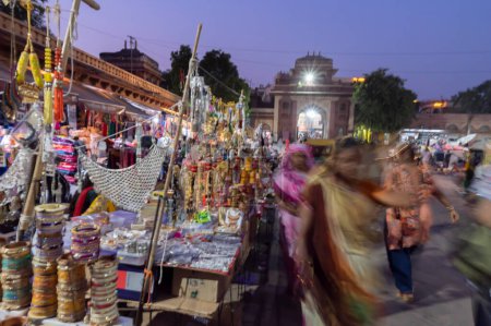 Téléchargez les photos : Jodhpur, Rajasthan, Inde - 19.10.2019 : Des ornements, bracelets, bijoux plaqués or et argent sont vendus au célèbre marché de Sardar et à la tour de l'horloge ghar de Ghanta dans l'après-midi. Heure bleue. - en image libre de droit