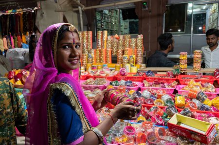 Photo for Jodhpur, Rajasthan, India - 18.10.2019 : Smiling Rajasthani woman trying out colorful bangles. Bangles being sold at famous Sardar Market and Ghanta ghar Clock tower in Jodhpur, Rajasthan, India. - Royalty Free Image