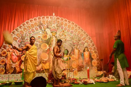 Foto de Howrah, India - 13 de octubre de 2021: Los sacerdotes hindúes adoran a la Diosa Durga con panchapradip, ghanta, chamor y abanico de manos. Ashtami puja aarati - ritual sagrado Durga Puja - disparo en la noche. - Imagen libre de derechos