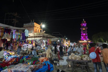 Photo for Jodhpur, Rajasthan, India - 20.10.2019 : Rajasthani womens clothes being sold at Famous Sardar Market and Ghanta ghar Clock tower in the evening. - Royalty Free Image