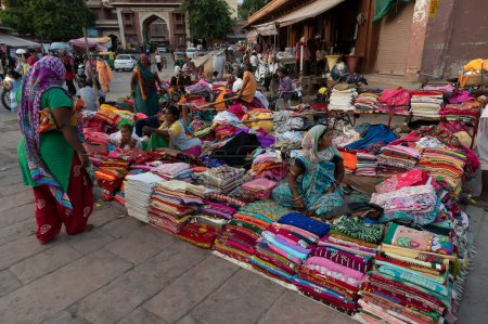 Téléchargez les photos : Jodhpur, Rajasthan, Inde - 20.10.2019 : Des vêtements pour femmes Rajasthani vendus au célèbre marché de Sardar et à la tour de l'horloge ghar de Ghanta le soir. - en image libre de droit