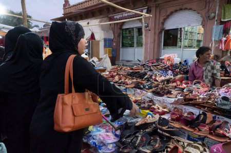 Photo for Jodhpur, Rajasthan, India - 20.10.2019 : Modern Muslim women with hijab, cloth wrapping their head, neck and shoulder are buying colorful Rajsathani ladies shoes at famous Sardar Market in Jodhpur. - Royalty Free Image