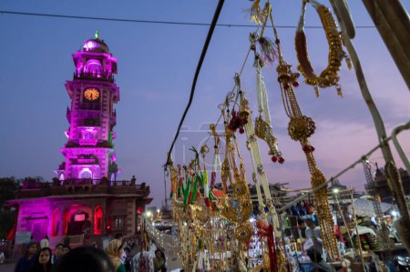 Téléchargez les photos : Jodhpur, Rajasthan, Inde - 19.10.2019 : Des ornements plaqués or et argent sont vendus au célèbre marché de Sardar et à la tour de l'horloge ghar de Ghanta dans l'après-midi. Heure bleue. - en image libre de droit