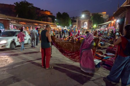 Photo for Jodhpur, Rajasthan, India - 19.10.2019 : Foreigners buying Rajasthani womens clothes being sold at Famous Sardar Market and Ghanta ghar Clock tower in the evening. - Royalty Free Image