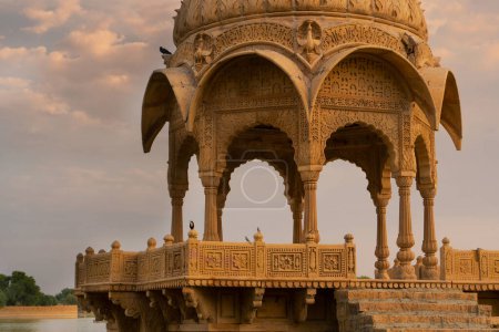 Foto de Close up view of Chhatris and shrines of hindu Gods and goddesses at Gadisar lake, Jaisalmer, Rajasthan, India. Indo-Islamic architecture , sun set in the sky at the Gadisar lake. - Imagen libre de derechos