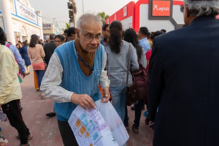 Téléchargez les photos : Kolkata, West Bengal, India - 2nd February 2020 : Old book lover man searching for favourite books with book fair ground map in hand at Kolkata Bookfair. Biggest book fair of the world. - en image libre de droit