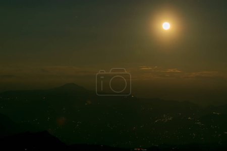 Photo for Rise of the orange moon, also known as the harvest moon or the hunter's moon, over the night sky at Sikkim, India. Moon orange due to atmosphere.Sikkim at night is seen below with Himalayan mountains. - Royalty Free Image