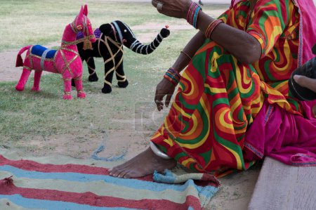 Photo for Old aged Rajasthani woman selling hand made Rajaasthani colourful dolls of horse and elephant. Rajasthan is famous for its colors and the little dolls represent colors spread all across Rajasthan. - Royalty Free Image