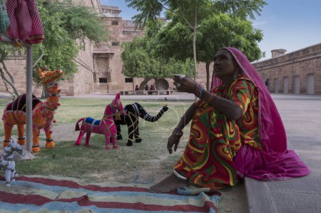 Photo for Jodhpur, Rajasthan, India - 19th October 2019 : Old aged Rajasthani woman selling hand made Rajaasthani colourful dolls of horse and elephant. Rajasthan is famous for its vibrant colors all across. - Royalty Free Image